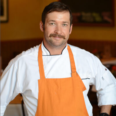Man with a moustache wearing an orange apron