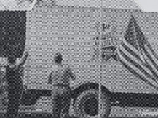 Black and white photo of an american flag in front of a truck with a "Manda's" logo